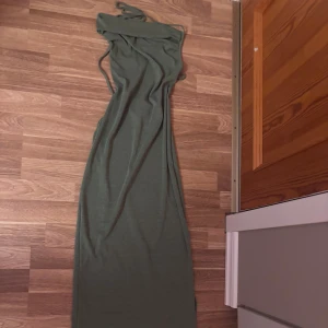 Grön långklänning med snörning - Snygg grön långklänning med smala axelband och snörning i ryggen. Klänningen har en figurnära passform och är tillverkad i ett mjukt, stretchigt material som känns skönt mot huden. Perfekt för dig som vill ha en stilren och enkel look med en twist.