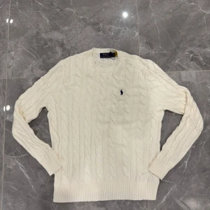 Vit kabelstickad tröja Polo Ralph Lauren - Säljer en vit kabelstickad tröja från Polo Ralph Lauren i storlek M. Tröjan har rund hals, ribbade muddar och det klassiska broderade Polo-logot på bröstet. Perfekt för dig som gillar clean och stilren look med premiumkänsla.