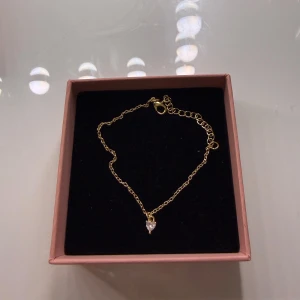 Guldarmband med hjärtformad pärla - Snyggt och tunt guldarmband med en liten hjärtformad pärla som hänger i mitten. Kedjan är finlänkad och har justerbar längd med karbinlås. Perfekt för dig som gillar stilrena och söta detaljer.