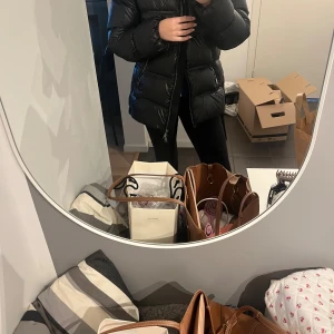 Svart pufferjacka med huva - Säljer min superfina jacka, dunjacka med huva och tvåvägsdragkedja. Jackan har en glansig yta och är riktigt fluffig, perfekt för kalla dagar. Den har långa ärmar och en snygg passform. Passar dig som gillar streetstyle och vill hålla dig varm. Som ny. Nypris 2000kr