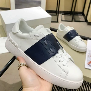 Valentino Garavani vita sneakers med blå detalj - Snygga vita sneakers från Valentino Garavani med bred mörkblå rem över vristen och coola nitar på hälen. Skorna har snörning, rund tå och är tillverkade i skinn. Sulan har ett unikt mönster med pyramidformade detaljer. Perfekta för dig som gillar exklusiv streetstyle.