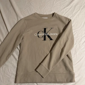 Beige sweatshirt från Calvin Klein Jeans - Snygg beige sweatshirt från Calvin Klein Jeans med stort svart CK-tryck och vit logga på bröstet. Size M men passar dig som har S jätte bra