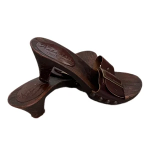 Bruna sandaler med klack från Andrea Cortés - Snygga sandaler från Andrea Cortés i mörkbrunt trä och skinn. De har en bred rem i brunt läder med en stor mässingsfärgad spänne och nitar på sidorna. Klack i trä ger en cool retrovibe och passar perfekt till sommarens outfits.