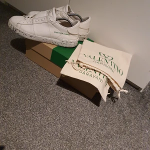 Valentino Garavani vita sneakers - Snygga vita sneakers från Valentino Garavani med svartstänkt sula och diskret logga på plösen. Skorna har snörning och texten 'OPEN FOR A CHANGE' på sidan. Tillverkade i skinn och levereras med originalbox och allt OG medföljer litet skrapmärke på vänster sko men märks inte vid användning då det är på insidan nya sulor i. Inköpta nya i fjol skick 7/10 kan gå ner i pris vid snabb affär storlek 42