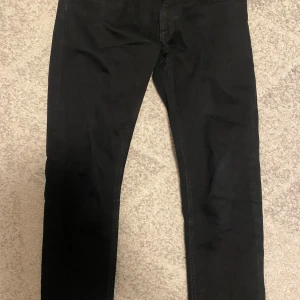 Svarta Nudie Jeans - Svarta jeans från Nudie Jeans med klassisk femficksdesign och smal passform. Jeansen har svarta sömmar, Nudie Jeans-logga på bakfickan och knapp med märkets namn. Tillverkade i stretchig bomullsdenim för en bekväm känsla.