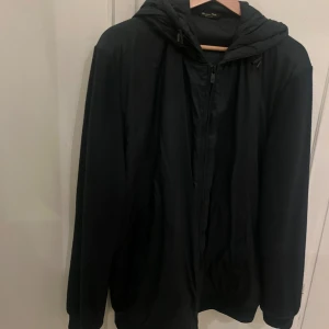 Mörkblå/svart cardigan från Massimo Dutti - Mörkblå/svart cardigan med huva från Massimo Dutti. Jackan har dragkedja framtill och är tillverkad i en blandning av ull och syntet. Supersnygg och i mycket bra skick. 