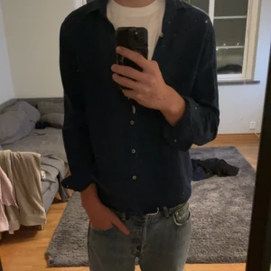 Mörkblå linneskjorta från Dressmann - Snygg mörkblå skjorta från Dressmann i linnemix. Klassisk krage, knäppning framtill och en bröstficka. Skjortan har lång ärm och en clean look som passar till jeans eller chinos.