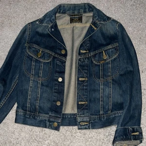 Mörkblå jeansjacka från Lee - Oanvänd snygg mörkblå jeansjacka från Lee med klassiska guldfärgade knappar och kontrastsömmar. Jackan är croppad och har två bröstfickor med lock och knapp, samt långa ärmar med knapp vid mudden. Perfekt för dig som gillar en tidlös och cool stil. Nypris är 1200kr! Mitt pris 600kr då den är helt defektfri och i nyskick! Storlek M men liten i storleken! Skicka gärna prisförslag🙏🏽