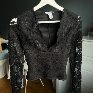 Svart spetstopp  - Svart topp med spets i storlek S med långärmade spetsärmar och v-ringad front. Slutsåld på hemsidan. Perfekt som festtröja eller till nyår!