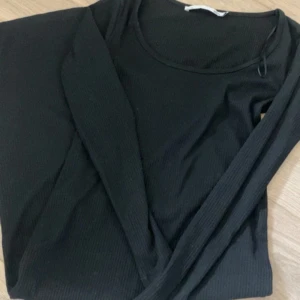 Svart ribbad långärmad klänning - En svart, ribbad långärmad klänning med rund halsringning. Klänningen har en enkel och stilren design med smal passform och är tillverkad i ett stretchigt material som sitter snyggt på kroppen. Perfekt för dig som gillar minimalistisk stil.