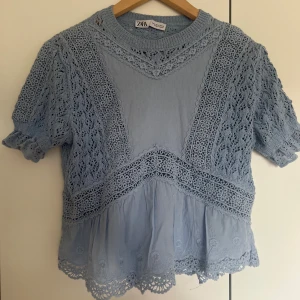 Blå spetsblus från Zara - Supersöt ljusblå blus från Zara med korta ärmar och detaljerad spets. Blusen har rund hals, volangkant nedtill och broderad. Storlek s. Helt oandvänd bara testad. 