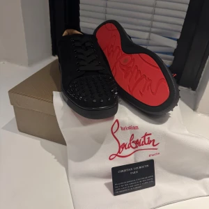 Christian Louboutin svarta sneakers med nitar - Svarta sneakers från Christian Louboutin med mattsvarta nitar på tån och ikoniska röda sulor. Skorna har snörning, rund tå och är tillverkade i mocka med läderdetaljer. Perfekt för dig som vill sticka ut med en lyxig och edgy stil.