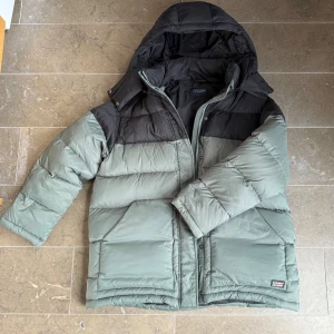  pufferjacka Lexington  - Säljer en grön och svart pufferjacka från Lexington i storlek L. Jackan har huva, två stora fickor och Lexingtons logga på bröstet. Fylld med syntetmaterial och har dragkedja framtill. Perfekt för kalla dagar och har en schysst oversized vibe.