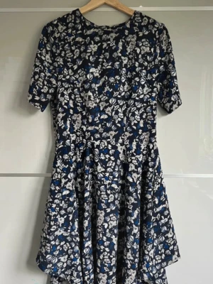 Blommig kortklänning från H&M - Supersöt kortklänning från H&M i marinblått med vitt och blått blommönster. Klänningen har rund hals, korta ärmar och ett mjukt, följsamt tyg som ger en skön känsla. Perfekt för dig som gillar en feminin och fräsch stil.