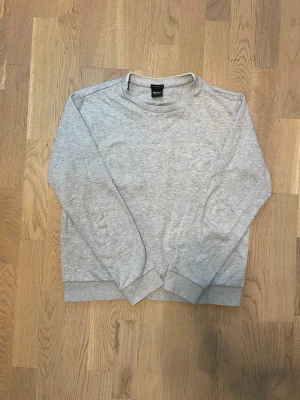 Ljusgrå sweatshirt från BOSS - Säljer en ljusgrå sweatshirt från BOSS med diskret broderad logga på bröstet. Tröjan har rund hals, långa ärmar och ribbade muddar vid ärmslut och nederkant. Tröjan är i storlek M men är faktiskt S eller XS. Hör av dig vid intresse, pris kan diskuteras!