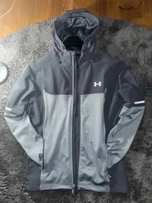 Under Armour Vindjacka - Snygg grå vindjacka från Under Armour. Ny pris: 1350kr, Mitt pris: 800kr. Använd några gånger men det finns inga fel med den och är precis som helt ny. Tveka inte att ställa frågor!