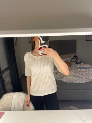 Vit stickad topp med puffärm - Säljer en vit stickad topp med kort ärm. Tröjan har en rund halsringning och ett snyggt, strukturerat mönster i stickat. 