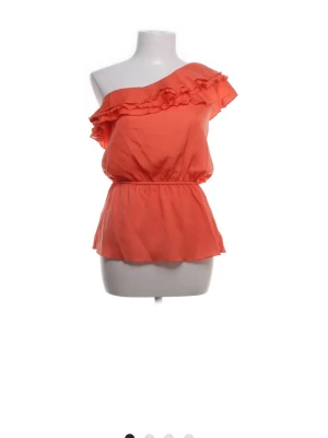 Korallfärgad omlott-top från Amisu - Säljer en snygg korallfärgad omlott-top från Amisu i storlek XS. Toppen har oneshoulder-design med volangdetaljer längs halsringningen och ett elastiskt midjeband som ger en feminin siluett. Perfekt för sommarens alla tillfällen!