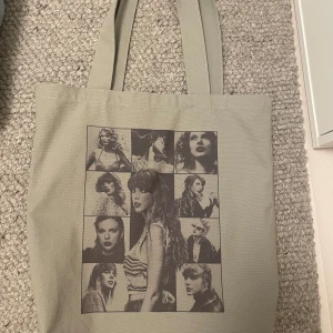 Tote Bag | THE ERAS TOUR. - [OFFICIELL MERCH; Köpt på Taylor’s konsert i sthlm]. Grå tote bag i med tryck av Taylor Swift och album från The Eras Tour på ena sidan och turnéstäder på andra sidan. Väskan har två långa handtag och är perfekt för att bära med sig allt man behöver till skolan eller stan.