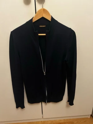 Svart kofta med dragkedja från Stenströms - Snygg svart kofta från Stenströms med stilren design och hel dragkedja framtill. Koftan har långärmade smala ärmar och ribbad krage. Materialet känns mjukt och är troligtvis bomull eller ull, perfekt för lager på lager under höst och vinter.