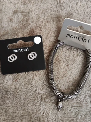 Nya örhängen och nytt armband  - Smycken från Montini, inklusive ett par örhängen med glittriga detaljer och ett armband i silverfärgad metall med döskalleberlock. Helt nya.