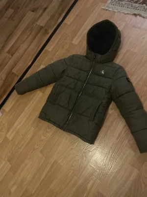 Olivgrön pufferjacka från Calvin klein - Fin, passar till allt. Den har skador lite hör o där men syns inte. Syns bara om man kollar noga