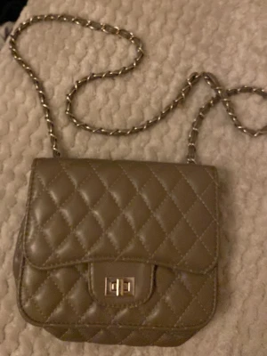 Beige quiltad axelväska med kedja - Säljer en beige axelväska med quiltat mönster och snygg kedjerem. Väskan har en klassisk fyrkantig form och ett metallspänne framtill. Perfekt storlek för det viktigaste och ger en cool vibe till din outfit.