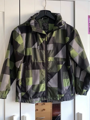 Grön och svart rutig vindjacka Warp - En fint regnjacka för barn och som ni ser på bilden har den inte så stora eller många skador/fläckar. 💕