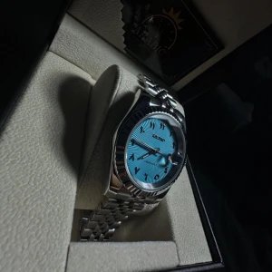 Seiko Mod Baby Blue Klocka - Säljer en stilren Seiko klocka med automatisk urverk, baby blur urtavla med arabiska siffror och datumvisning samt luminous handvisare. 39 mm klockan med ett klassiskt rundat silverfärgat boett och länkarmband i 904L stäl. Glas på bada sidorna gjort av safir vilket innebär att den är reptälig. Perfekt accessoar för dig som gillar snygga detaljer och modern design.