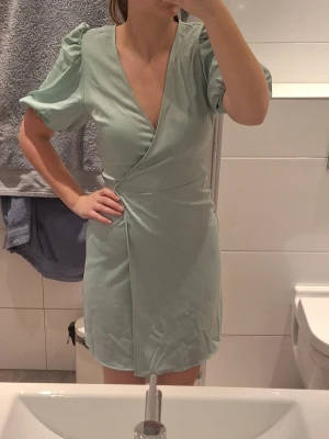 Ljusgrön omlottklänning Bik Bok XS - Supersöt ljusgrön omlottklänning från Bik Bok i storlek XS. Klänningen har puffiga korta ärmar, v-ringning och knytband i midjan. Perfekt för sommarens alla tillfällen och ger en fräsch och trendig look.