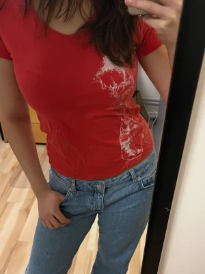 Röd t-shirt med vit print - Säljer en röd t-shirt med coolt vitt tryck på sidan. T-shirten har korta ärmar och sitter tight mot kroppen. Perfekt för dig som gillar färgstarka plagg med unik detalj framtill. Materialet känns mjukt och skönt mot huden.