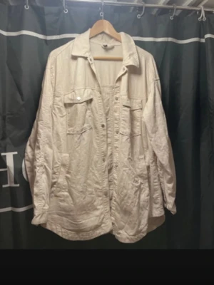 Beige overshirt från Divided H&M - Säljer en beige overshirt från Divided H&M i bomull. Jackan har klassisk krage, knappar framtill och två stora bröstfickor med lock. Perfekt att slänga över en hoodie eller t-shirt för en chill look. har en fläck på armen. Se bild två