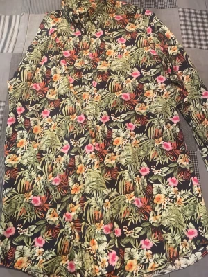 Blommig skjorta från Morris, S - Säljer en färgstark skjorta från Morris i storlek S med tropiskt blommigt mönster i grönt, orange, rosa och vitt. Skjortan har klassisk krage, knappar framtill och ett broderat emblem på bröstet. Perfekt för dig som gillar att sticka ut med din stil.