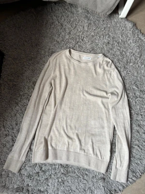 Beige stickad tröja från Jack & Jones - Säljer en stilren beige stickad tröja från Jack & Jones. Tröjan har rund hals, långa ärmar och ribbade muddar vid ärmslut och nederkant. Perfekt för lager-på-lager och enkel att matcha med jeans eller chinos.