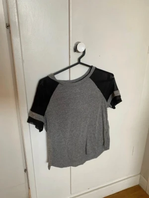 Grå t-shirt med meshdetaljer från H&M - Säljer en grå t-shirt från H&M Divided i storlek S. T-shirten har svarta meshdetaljer på axlar och ärmar, vilket ger en cool kontrast. Materialet är en mix av polyester och viskos, med mesh i polyamid och elastan. Perfekt för dig som gillar sportig och trendig stil.