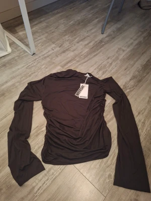 Mörkbrun asymmetrisk topp Weekday - Säljer en mörkbrun draperad topp från Weekday med asymmetrisk design och oneshoulder. Storlek L men passar mellan M och L. Köpt för ungefär 2 månader sedan aldrig använd! Bara provat en gång efter köp. Lapp finns kvar! Köpt för 300kr, Pris kan förhandlas!