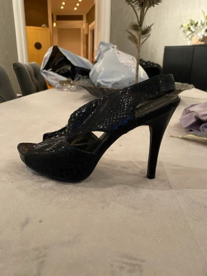 Klackskor | Moda Spana - Ett par jättefina svarta klackskor i ormskinn (fejk). De är från märket Moda Spana, vilket är väldigt dyrt! De är i använt, men bra skick! För mer info och bilder skriv privat!