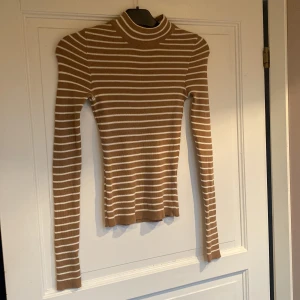 Halvpolo från Gina  - Beige vit randig halvpolo från Gina i nyskick, storlek M, den stretchar sig efter kroppen och sitter slim. 