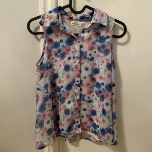 Armlösskjorta  - Vit armlösskjorta med blåa och rosa blommor på. Fint skick💙🩷