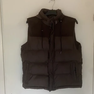 brun väst med luva - luva kan vikas in i en fika som sitter runt kragen