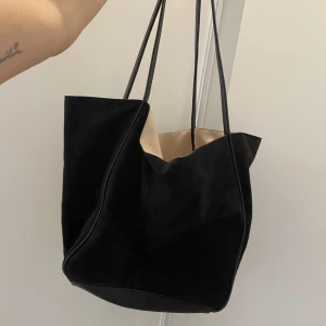 Handväska - En svart Handväska i Mocka, Använd fåtal gånger pga har 2st likadana. Rymmer en dator och massa mer utan problem! Lädersnören på insidan som man knyter ihop om man vill ha den stängd.🥰