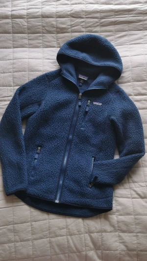 Patagonia Fleece pile jacket - Fleecetröja utan foder i Pile med luva. Fin mörkblå färg. Dammodell strl S. 100% polyester.  Den är använd, men väl omhändertagen. Har lite noppror på armbåge/underarm enligt bild, annars fint skick. Säljer pga har blivit för trång för mig. Nypris ca 1500