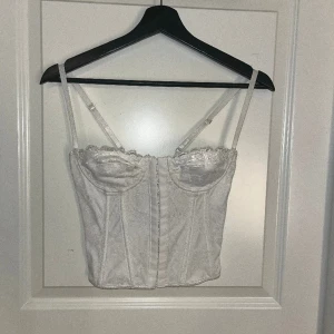 Korsett topp - En vit korsett topp i storlek XS. Den har spetts på utsidan, öppen snörning i rygggen och man knäpper den på framsidan :) 