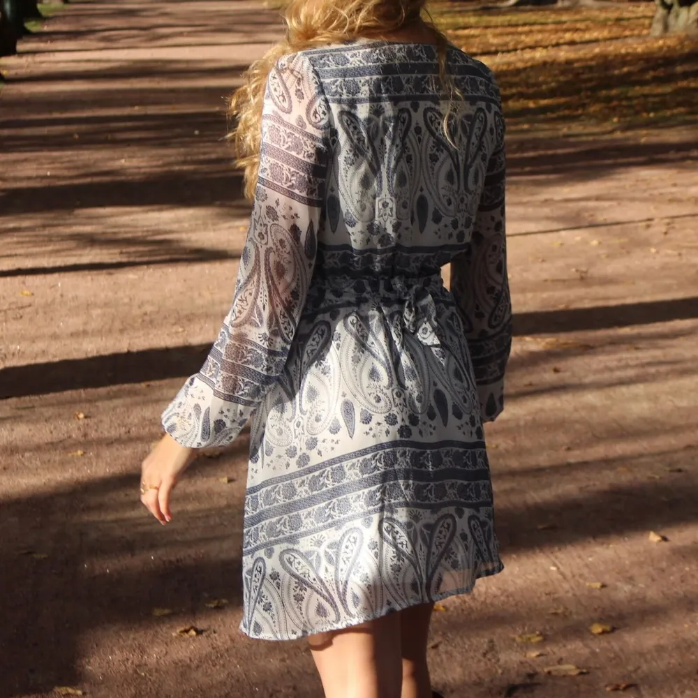 Beställningar görs via vår hemsida: thrifteddesign.one.   En blåmönstrad långärmad klänning med band runt midjan. . Klänningar.