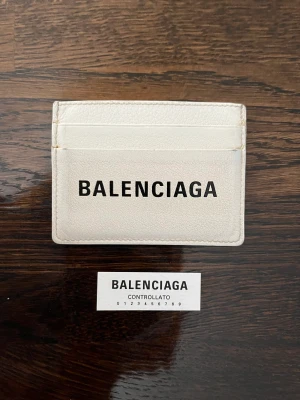 Balenciaga plånbok card holder - Köpt på Nathalie Schuterman 2018. Varsamt använd och i gott skick. Vit m svart logo. Tre fack per sida och fack för kontanter i mitten. Får plats fler kort per fack. Nypris 2895kr. Bild på kontrollkoden och prislapp i original. Pris kan diskuteras.