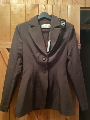 Brun blazer - Så fin blazer från Nelly som inte kommit till användning, lapparna kvar, storlek 32. Sitter fint format då den är lite ”figursydd” med 2 knappar fram (Nypris 699kr men är slutsåld)