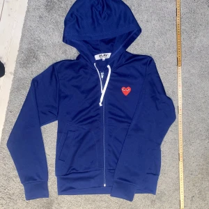 CDG Zip Hoodie - En CDG zip hoodie i helt nyskick. Knappt använd. Liten i storleken. Kan tänka mig att gå ned i pris vid smidig affär.