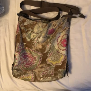 Grön/brun väska - Jätte söt väska med fint mönster. Knappt använd. Har ett snöre inuti väskan som man kopplar t.ex nycklar så man kan enkelt dra upp dem! 
