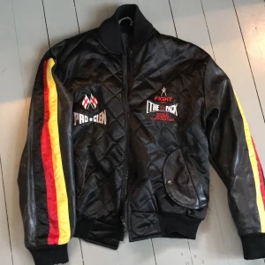 Svart bomberjacka - Cool svart bomberjacka med svarta, röda och gula ränder på bägge ärmar. Med dragkedja och fickor. 