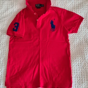 Polotröja, Ralph Lauren stl M - Ralph Lauren piké röd med blå big pony.  Nypris på outlet 899:-.  Mitt pris 290 inklusive frakt. Rökfritt, fläckfritt o djurfritt. Stl Medium. 